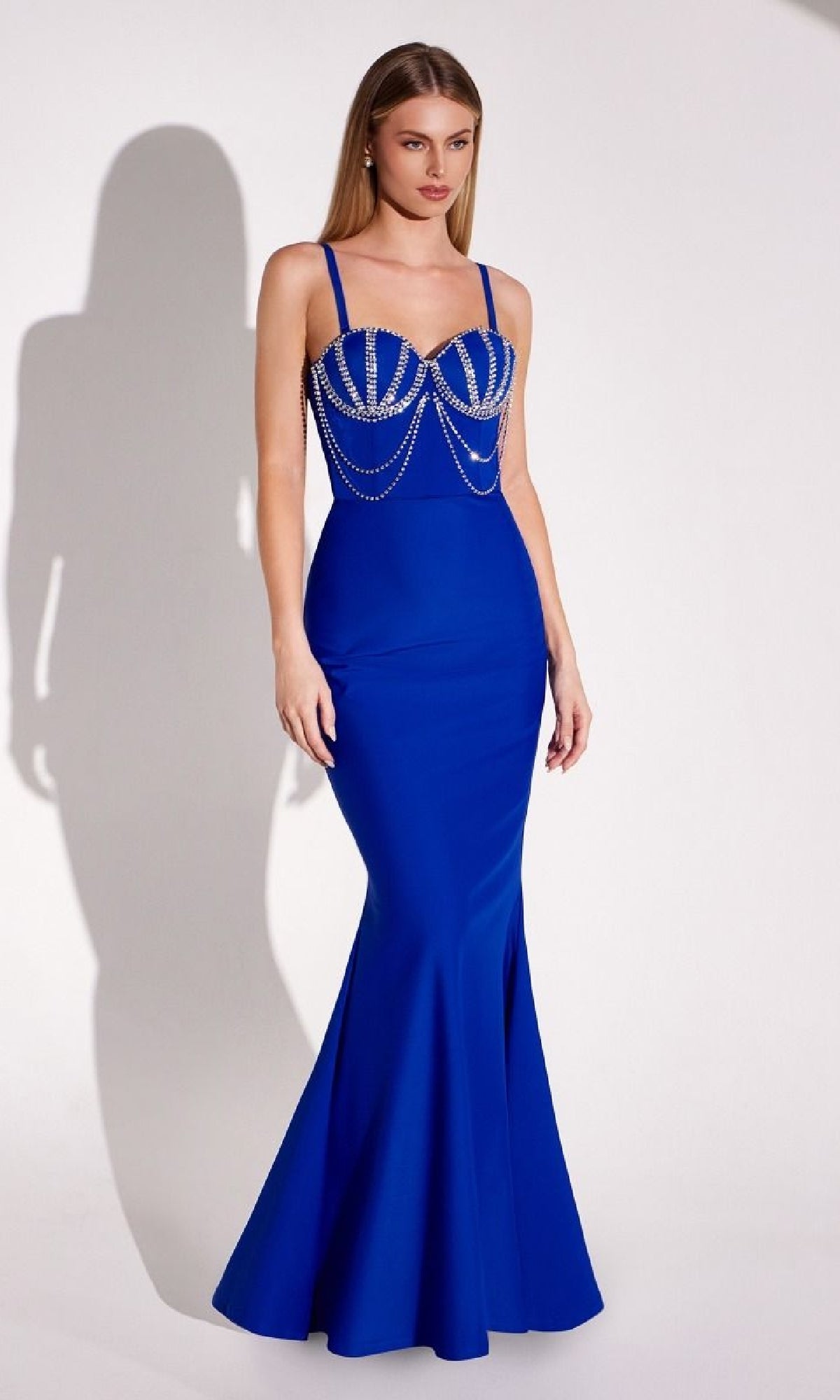 A woman stands against a plain backdrop wearing the Beaded-Bustier Long Prom Gown: Amoris T9003—a royal blue mermaid dress with a beaded bustier and thin straps.